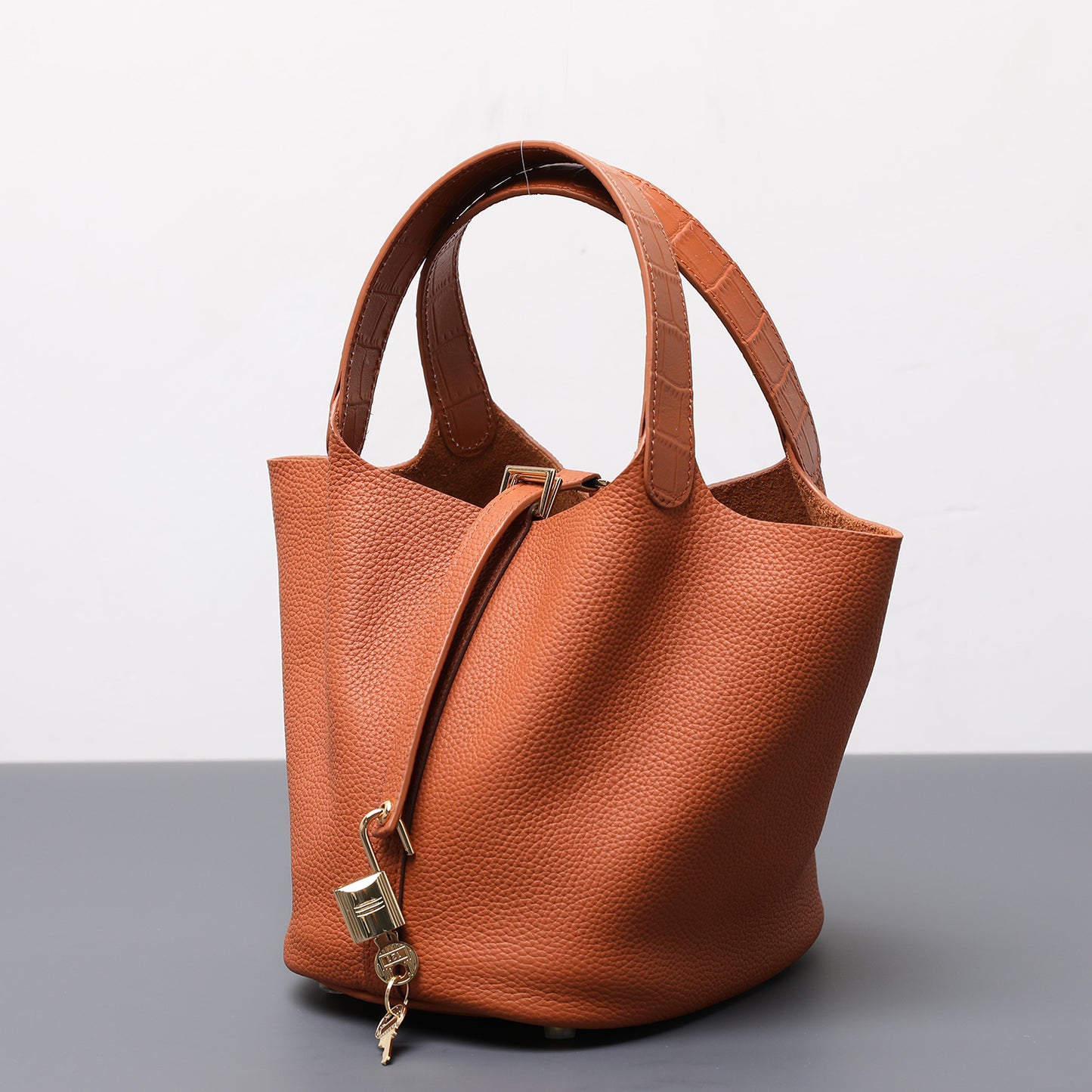 Brown leather handbag with a gold lock on a gray surface and light gray background