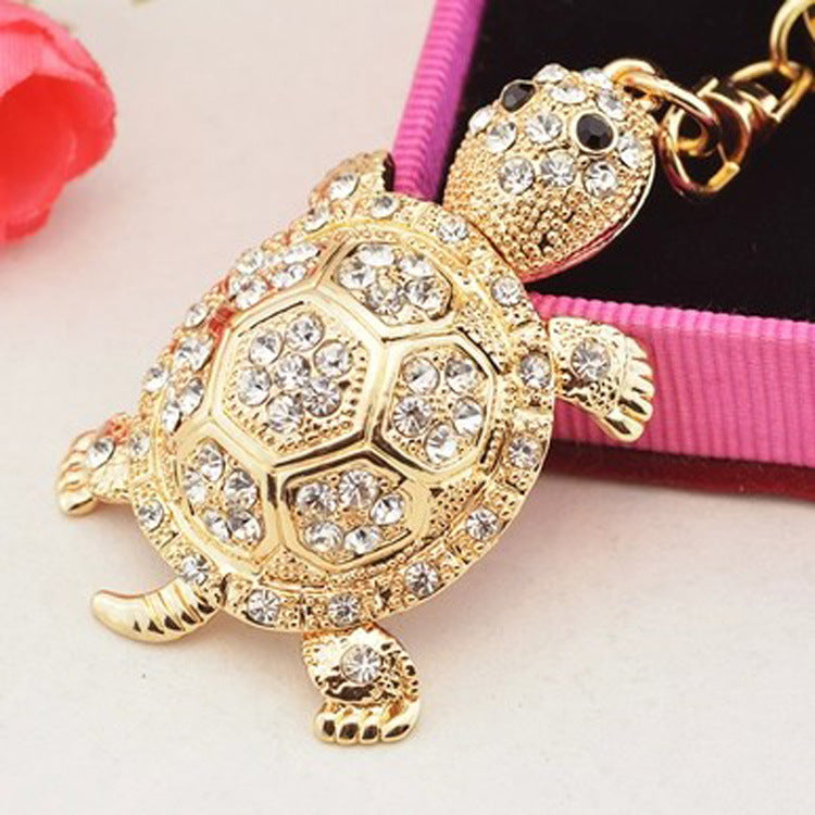 Gold turtle-shaped keychain with rhinestones on a pink background