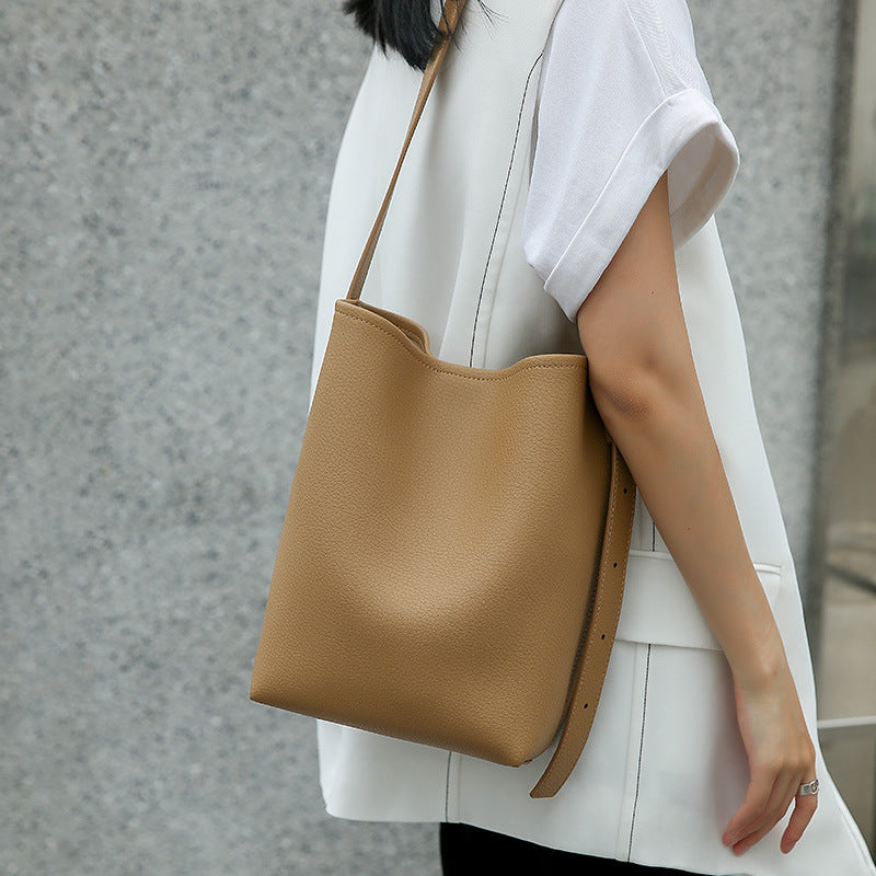 Person holding a brown leather tote bag against a neutral background