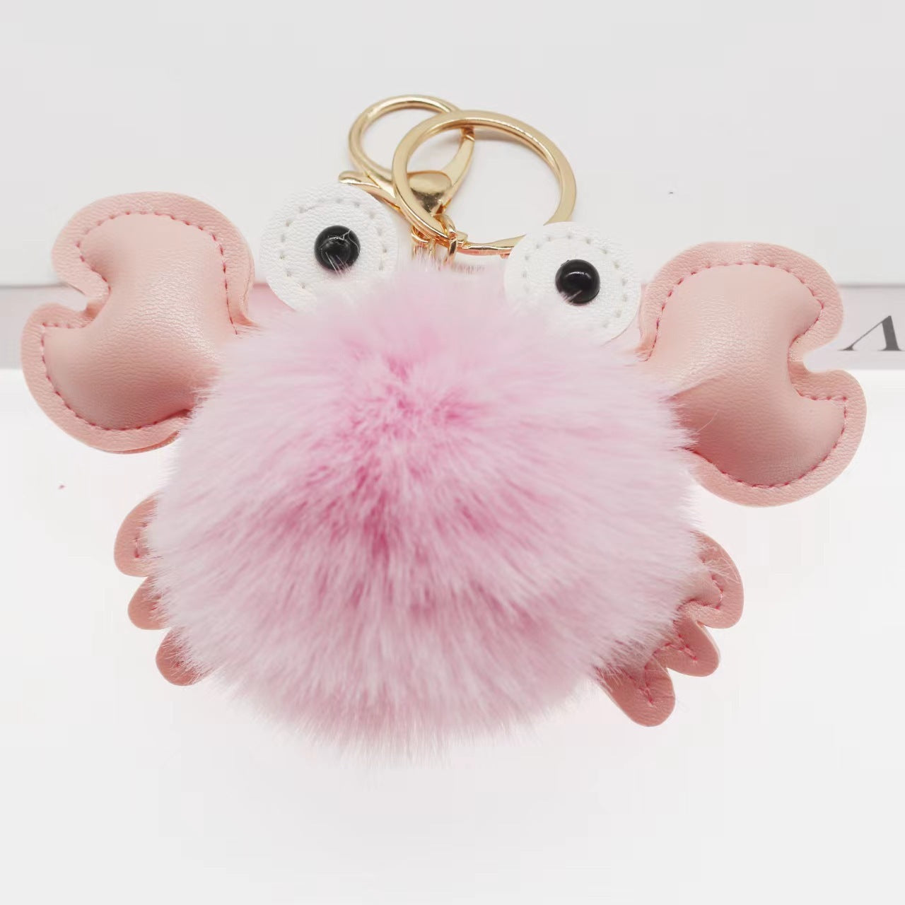 Pink crab-shaped keychain with a fluffy pink pom-pom