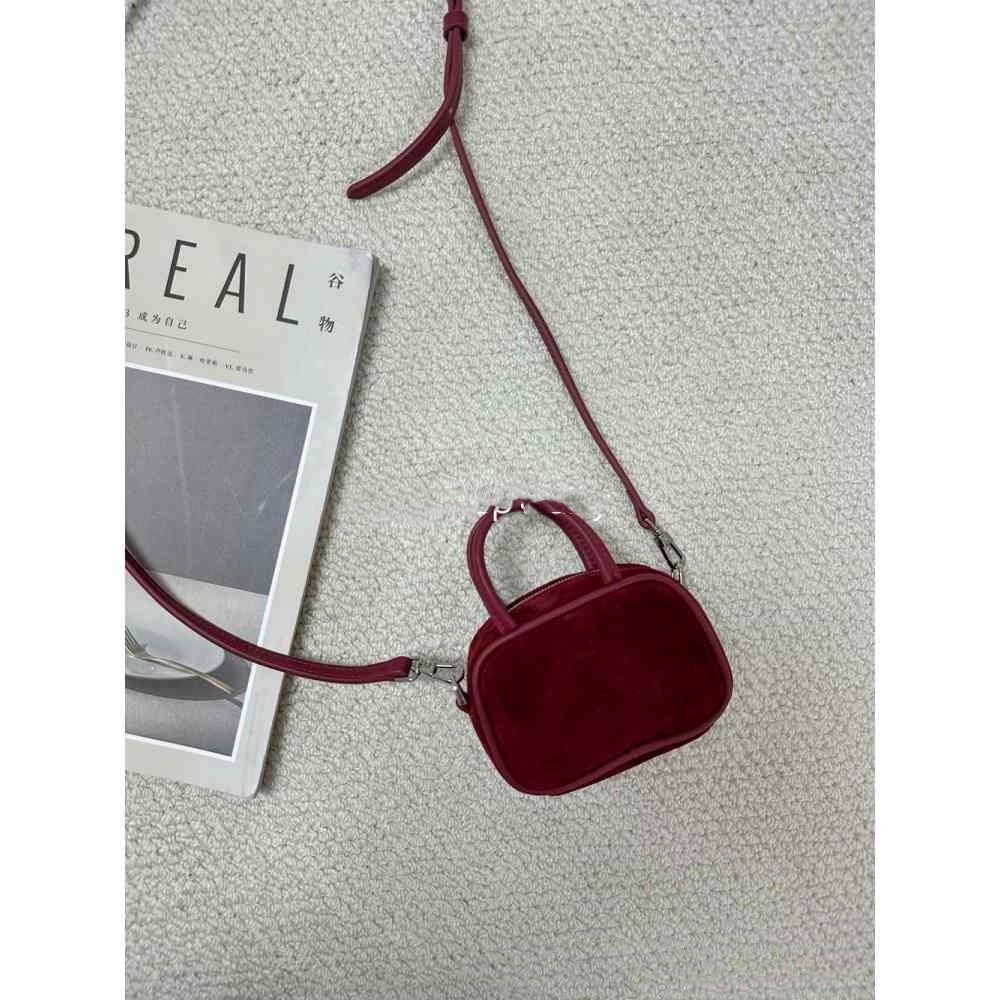 Red velvet handbag with a strap on a textured surface next to a magazine.