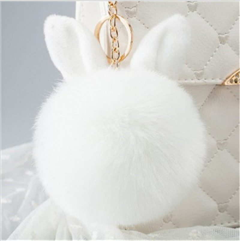 White fluffy keychain with gold chain on a textured surface