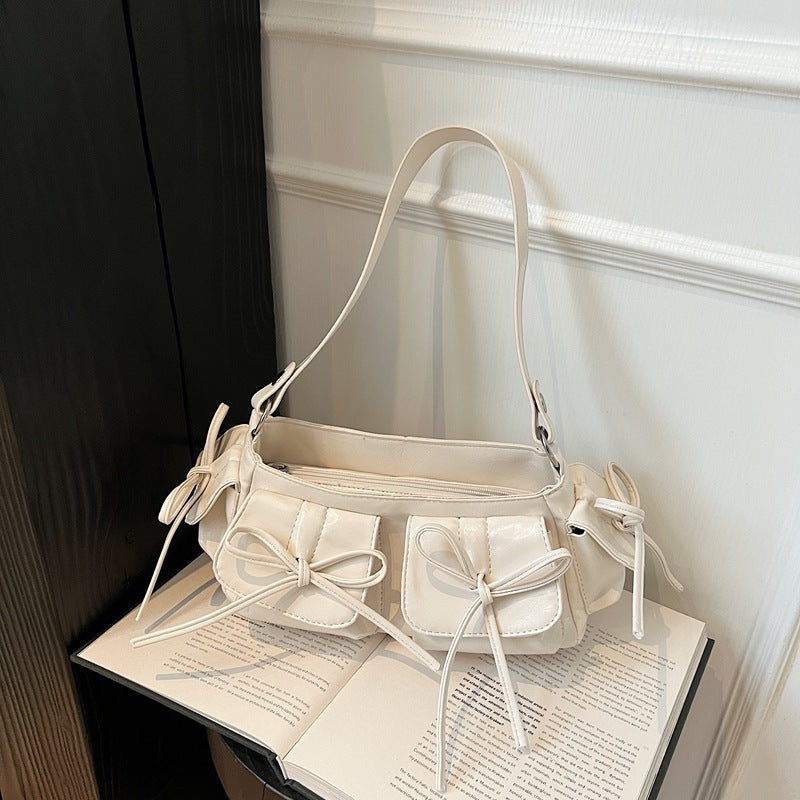 White handbag with bow details on an open book against a white wall.