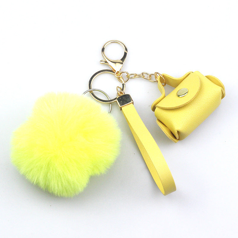 Yellow keychain with fluffy ball and small yellow bag on a white background