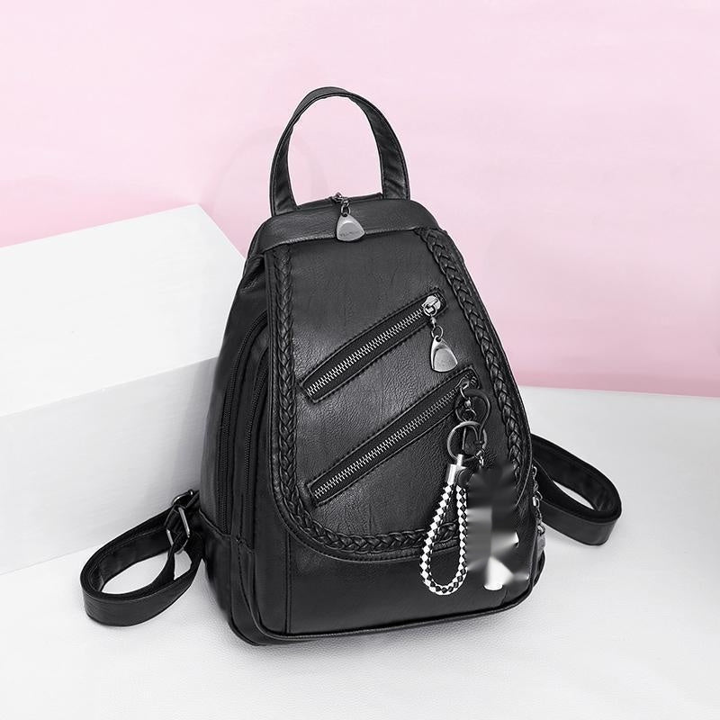 Black backpack with braided details and silver zippers on a white surface with a pink background
