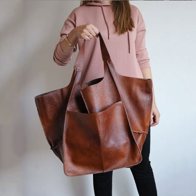 Person holding a large brown leather tote bag against a neutral background