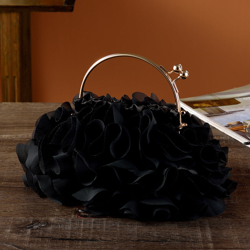 Black floral handbag with a gold handle on a wooden surface