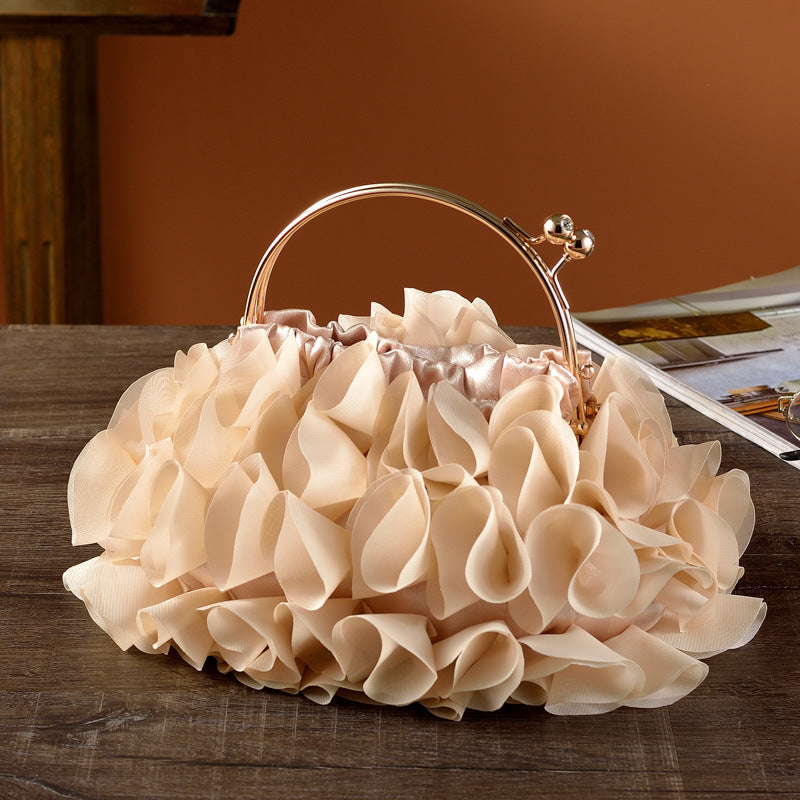 Beige ruffled handbag with a gold handle on a wooden surface.