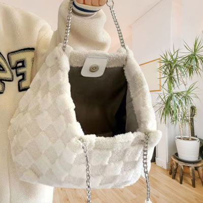 Person holding a textured white handbag with a chain strap indoors.