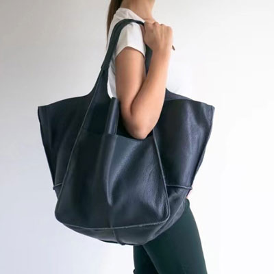 Person holding a large dark blue leather tote bag against a white background
