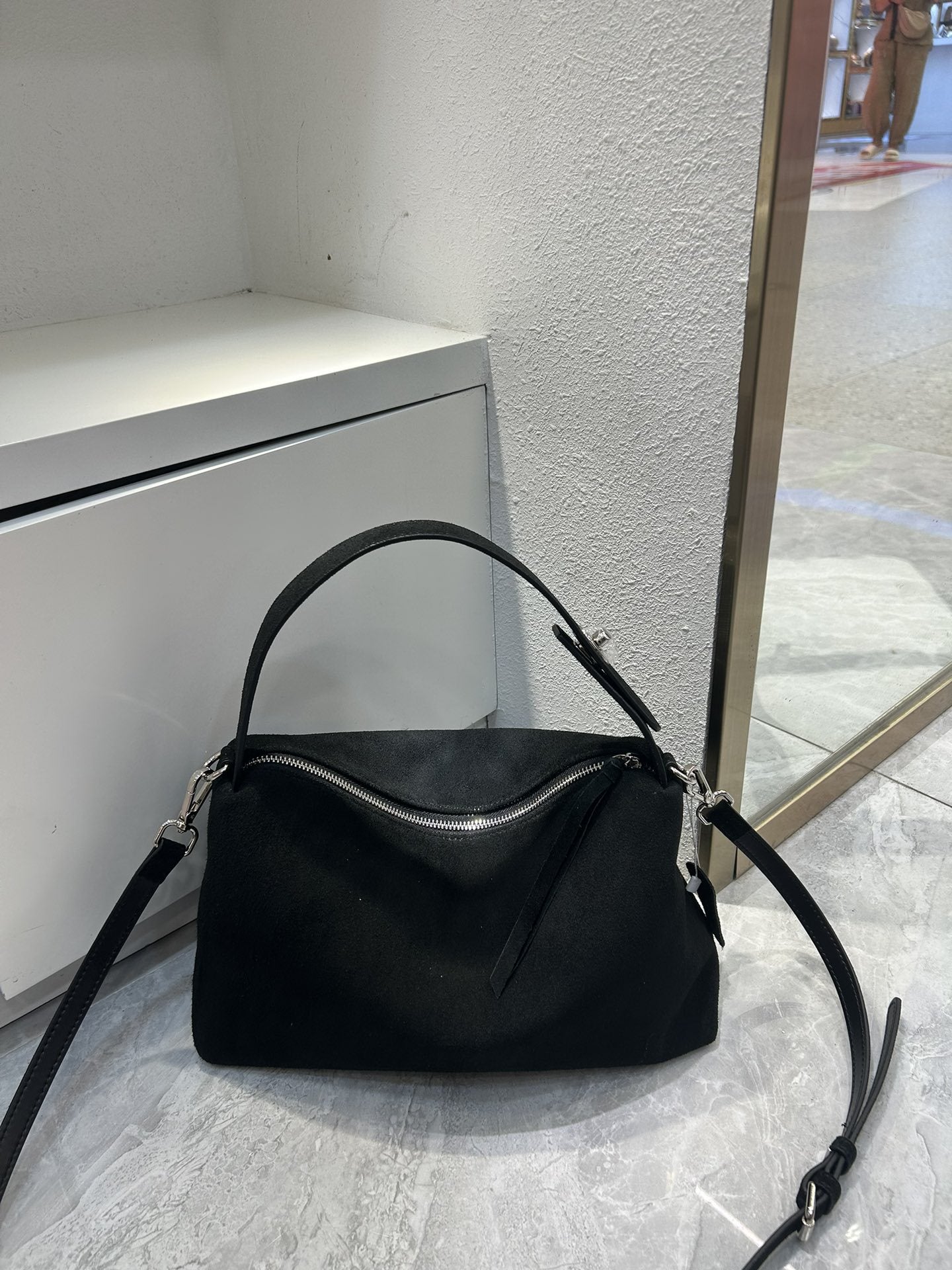 Black handbag on a marble floor with a neutral wall background