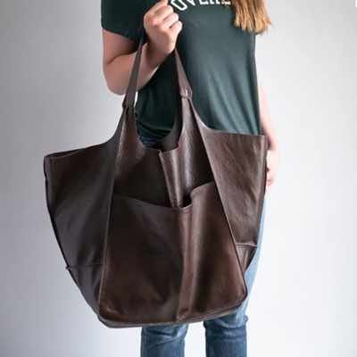 Person holding a large brown leather tote bag against a plain background
