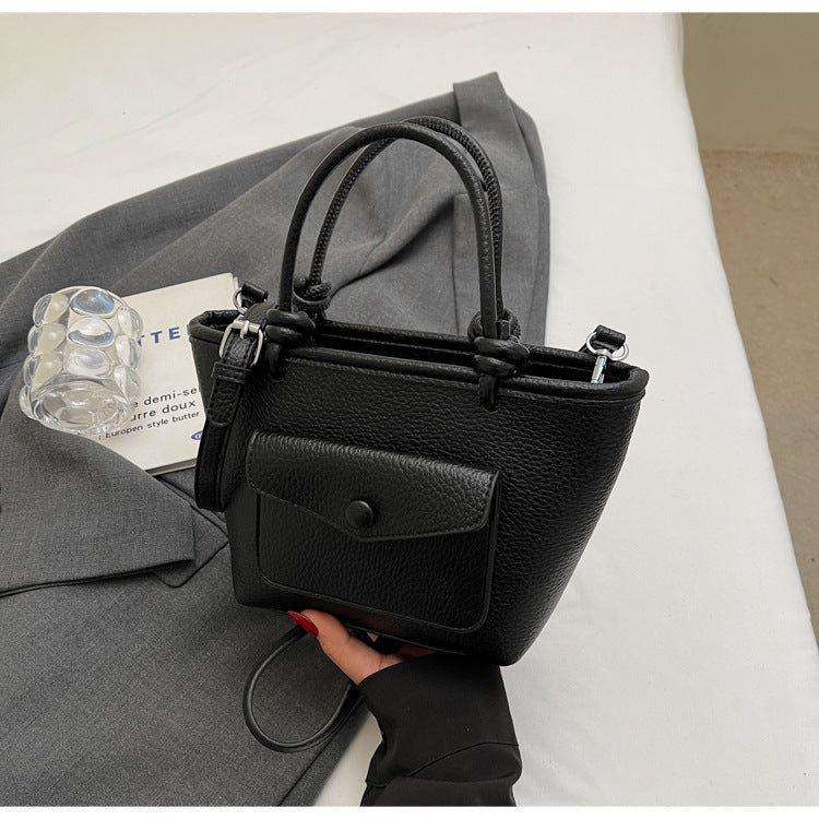 Black handbag held by a person with a gray coat and white surface in the background