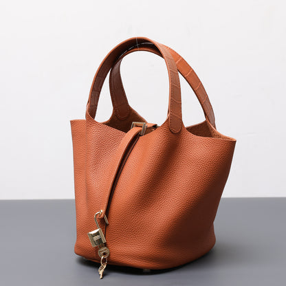 Brown leather handbag with a gold lock on a gray surface and light gray background