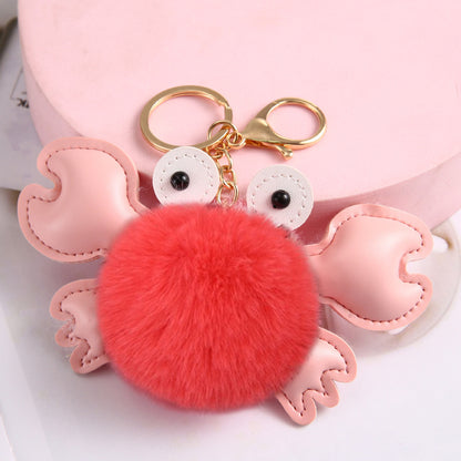 Pink crab-shaped keychain with a red pom-pom