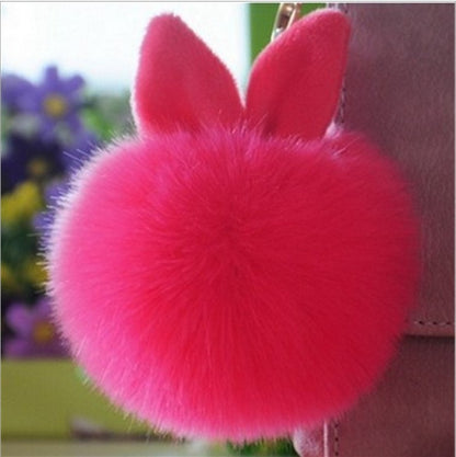 Pink fluffy keychain attached to a bag with a blurred floral
