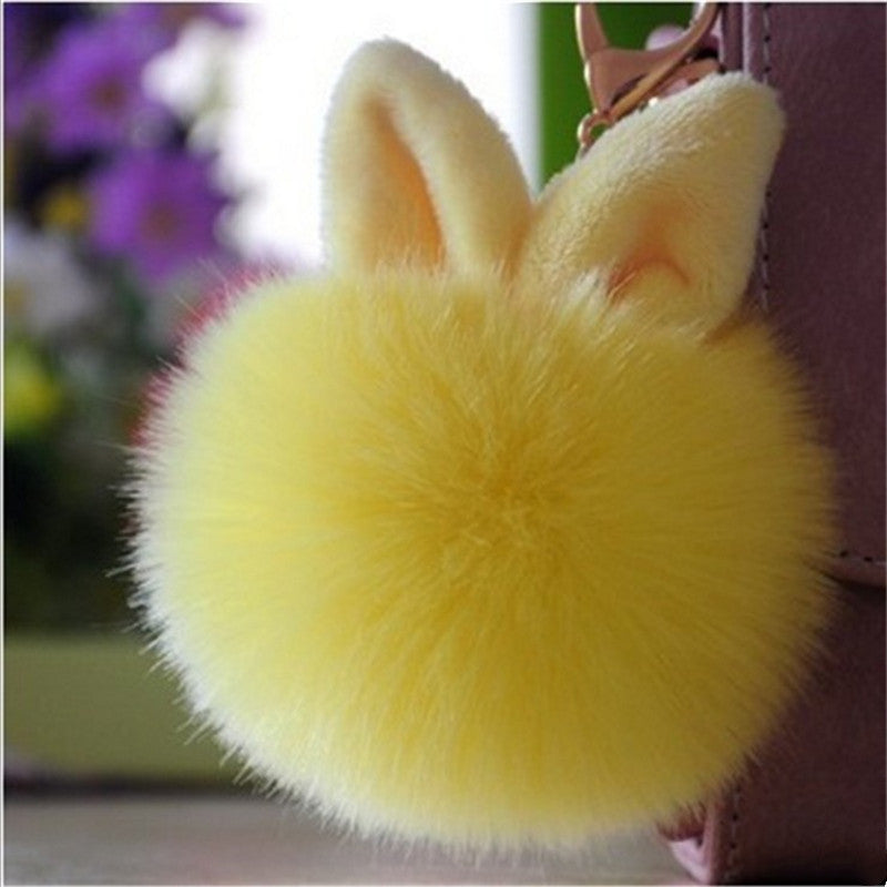 Yellow fluffy keychain with rabbit ears attached to a pink bag.