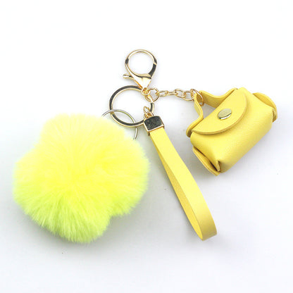 Yellow keychain with fluffy ball and small yellow bag on a white background