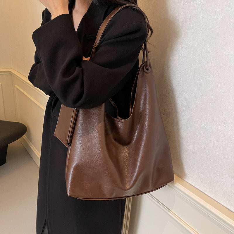 Person holding a brown leather handbag against a neutral wall.
