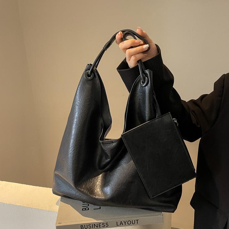 Person holding a black leather handbag against a neutral background