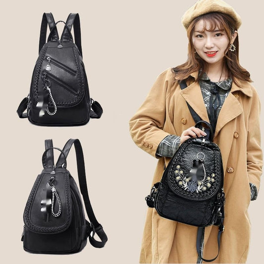 Woman holding a black backpack with decorative elements, wearing a beige coat and beret.