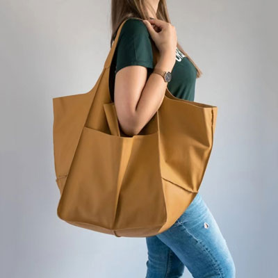Person holding a large brown tote bag against a plain background